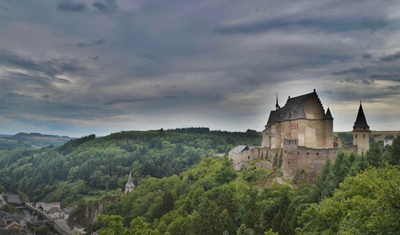 Burg in Luxemburg umringt von Wald mit dunklem Himmel