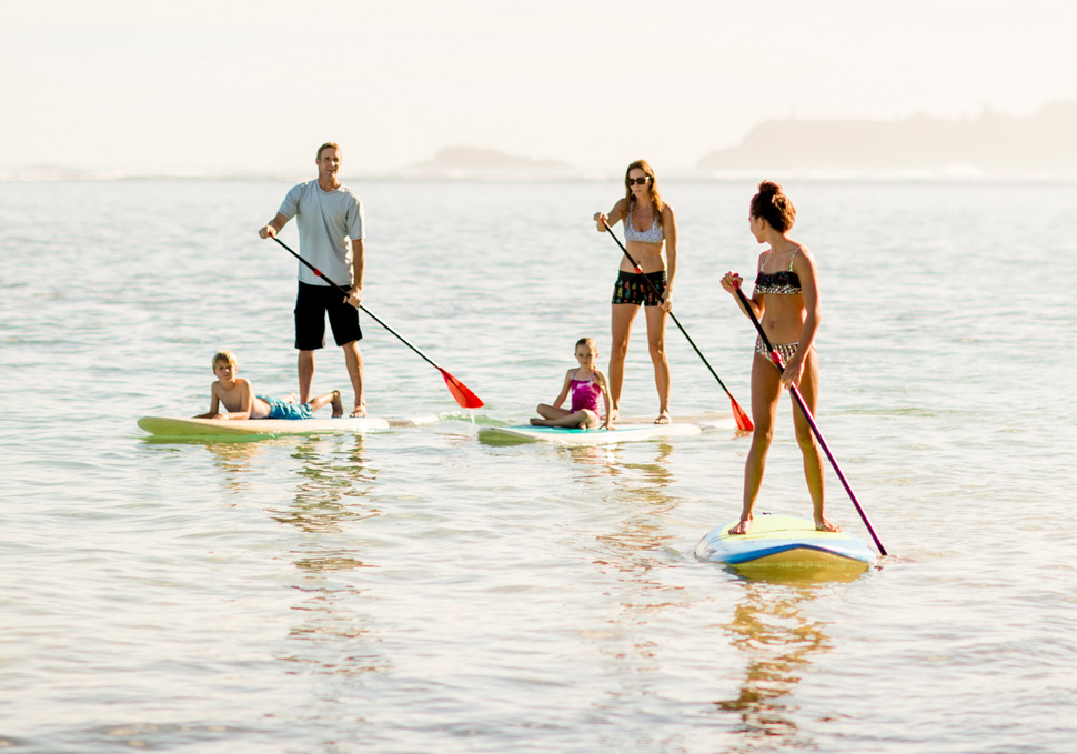 The host family and their au pair enjoying time together while doing stand up paddling